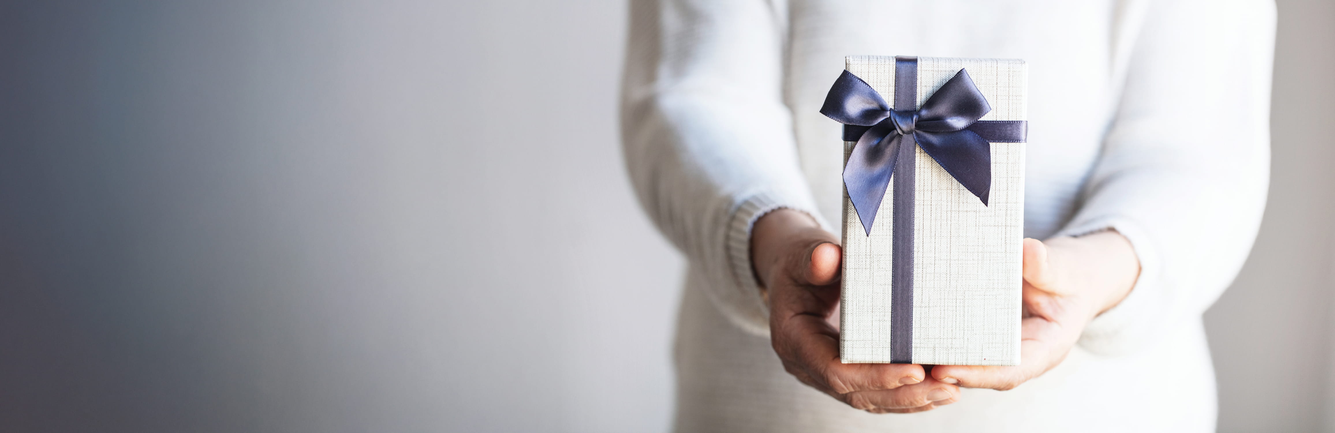 Hands offering a wrapped gift box with a navy ribbon.