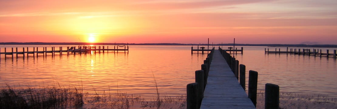 Sunset illuminates the sky with docks leading to a body of water in the foreground