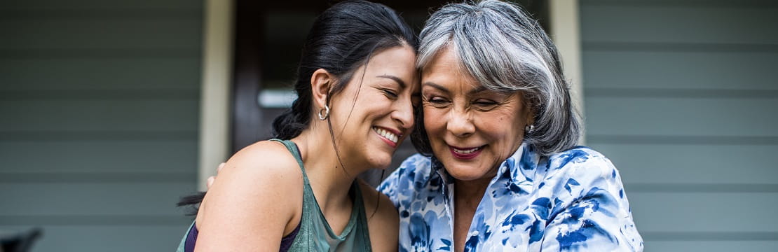Two women sitting on a front porch step smiling and hugging.
