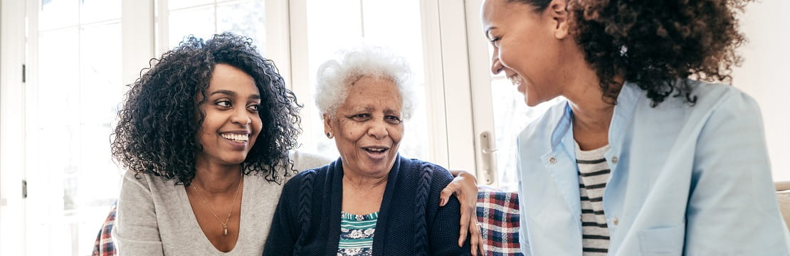 Two smiling women sit with their mother on a couch